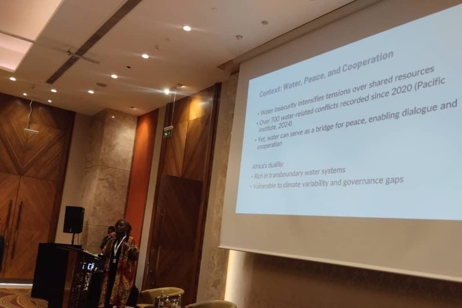 Njoki speaking at the Water Security Conference beside a slide on water, peace and cooperation.